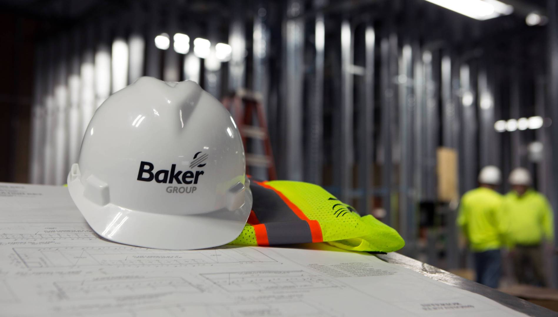 Hard hat and hi-vis vest on a table of blueprints.